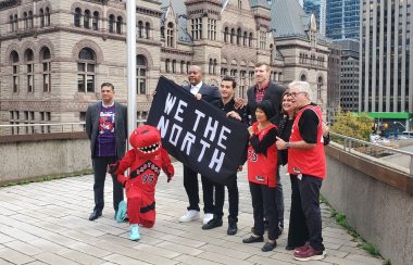 Mayor Olivia Chow and General Manager of the Toronto Raptors Bobby Webster pose with 'We The North' flag with former players of the team and mascot