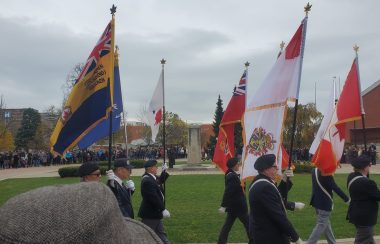 Six men walking with flags in military garb with a monument in the background