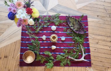 A blanket on the ground, covered with natural items such as antlers, flowers, and rocks.