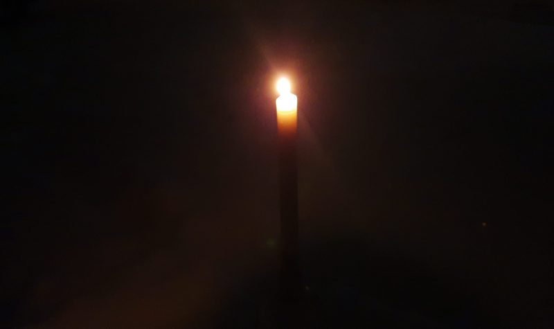 A candle burns in the dark on a snow covered surface. This lone candle symbolizes loneliness.