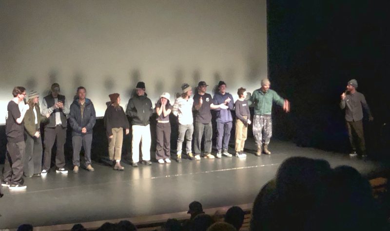 12 people in line on a stage under a blank screen.