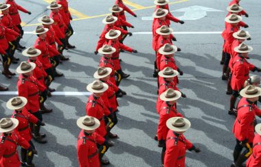 Rows of RCMP, dressed in red coasts and stetsons hats, marching on parademounted poolce