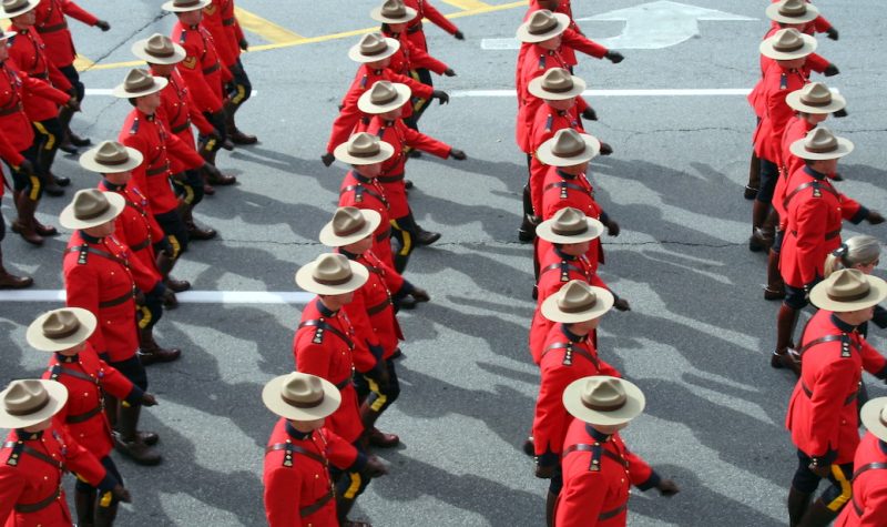 Rows of RCMP, dressed in red coasts and stetsons hats, marching on parademounted poolce