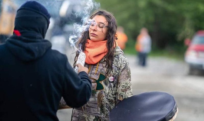 A man wearing black holds up smudging materials that smoke in front of a woman's face in a ceremony at Fairy Creek.