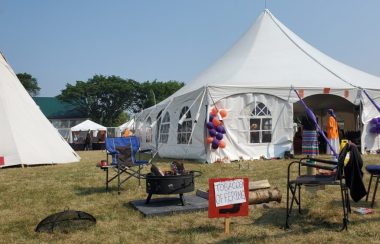 White tent with fire pit and a sign with smoke offering sign