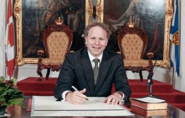 Homme politicien, assis à un bureau, signant des documents.