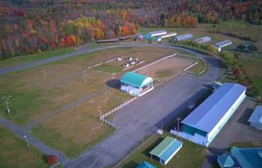 Pictured is a birds-eye view of the Brome Fair Grounds. The big stage, the bleachers, and some horse barns can be seen in the distance.