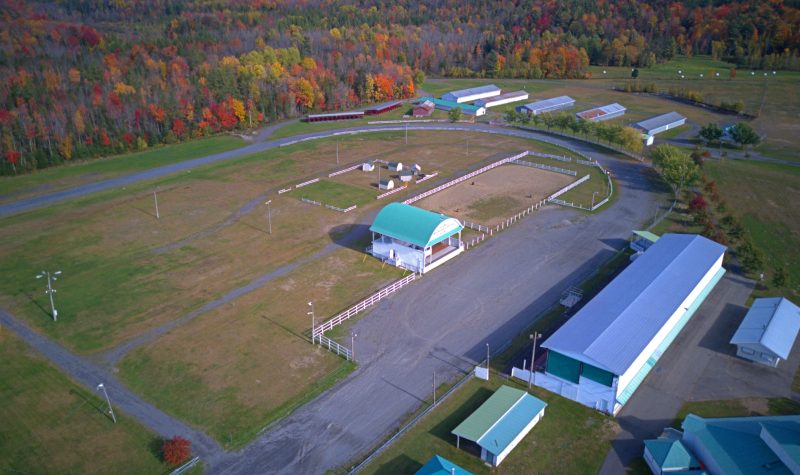 Pictured is a birds-eye view of the Brome Fair Grounds. The big stage, the bleachers, and some horse barns can be seen in the distance.
