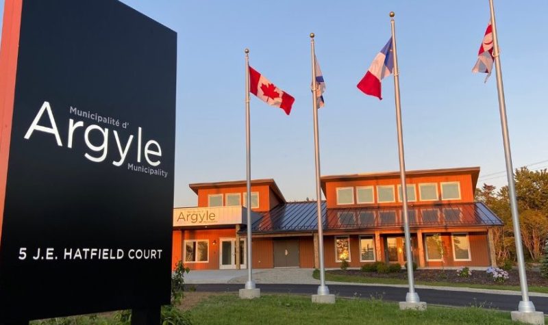 Les bureau municipaux avec devant le panneau de la municipalité et les 4 drapeaux, du Canada, de la Nouvelle-Ecosse, de l'Acadie et du peuple Micmaq. Il fait beau et le soleil est en train de se coucher avec des lumières chaudes