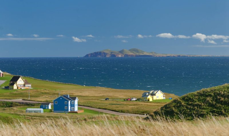 Trois maisons dans un champ en face de la mer avec une île en arrière plan.