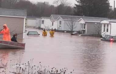 Pompiers évacuant des gens par bateau dans un parc de roulottes inondé par les pluies abondantes.