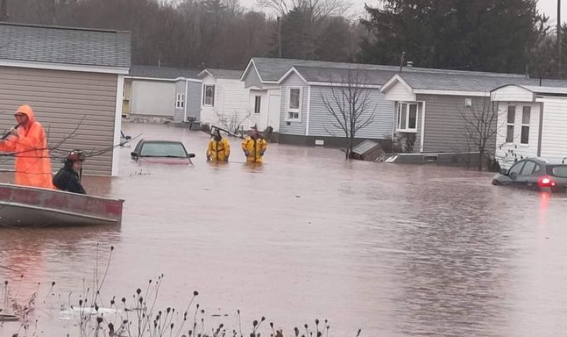 Pompiers évacuant des gens par bateau dans un parc de roulottes inondé par les pluies abondantes.