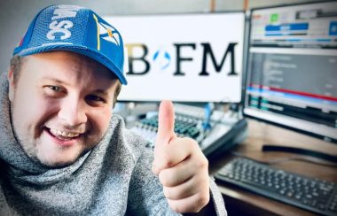 Homme avec chandail et casquette bleu en avant d'un ordinateur et d'équipement de radio.