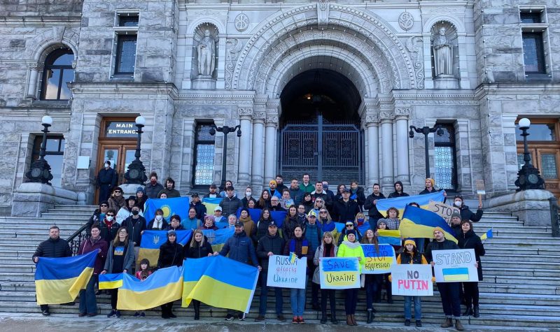 Une trentaine de personnes avec drapeaux de l'ukraine et pancartes devant le bâtiment de la législature