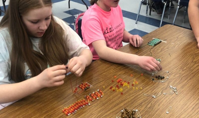 De jeunes filles assemblent des bracelets à l'aide de ficelles et de billes sur une table.