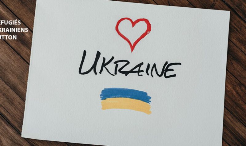 A piece of paper against a brown background that includes the word Ukraine, a red heart, and blue and yellow stripes. Réfugiés Ukrainiens Sutton is also included.