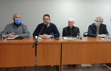 Four members of Sutton's town council sitting at a conference table. Director general Pascal Smith speaks into a microphone to present Tetra Tech's study to the public.