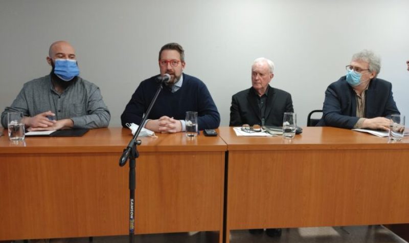 Four members of Sutton's town council sitting at a conference table. Director general Pascal Smith speaks into a microphone to present Tetra Tech's study to the public.