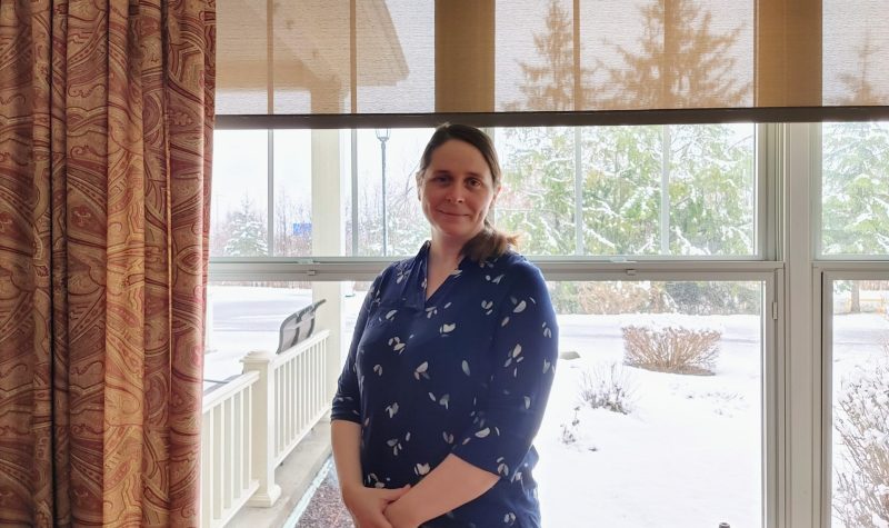 Pictured is executive director of Au Diapason Charlotte Evans standing in front of a window. She is wearing a navy blue floral shirt.