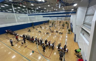 A line of archers in a gymnasium, shooting at fake animal targets, otherwise known as 3D archery.