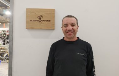 Pictured is co-founder of Pleins Rayons Stephan Marcoux. He is standing next to Pleins Rayons' welcome sign. The sign is made out of wood with the logo and name of organization engraved.