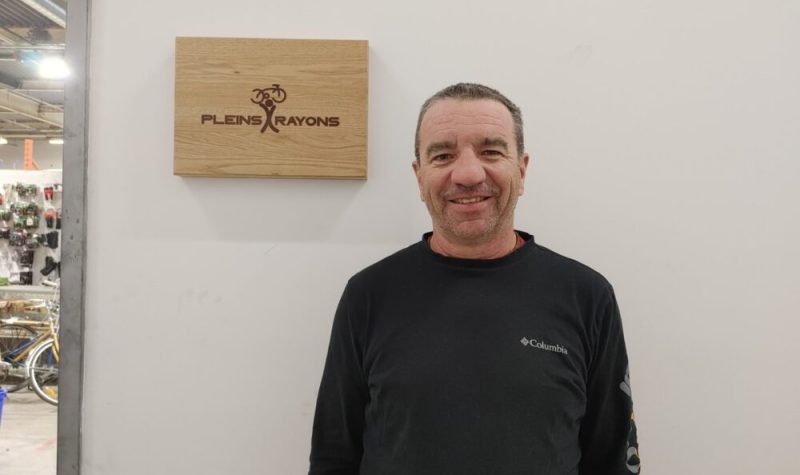 Pictured is co-founder of Pleins Rayons Stephan Marcoux. He is standing next to Pleins Rayons' welcome sign. The sign is made out of wood with the logo and name of organization engraved.