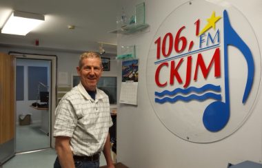 Un homme portant une chemise blanche en avant du logo de Radio CKJM.