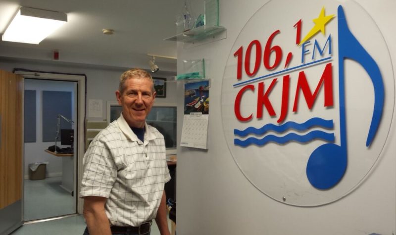 Un homme portant une chemise blanche en avant du logo de Radio CKJM.