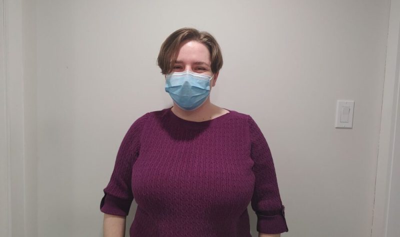 Pictured is Rachel Lambie, curator for the museum, standing against a white background wearing a bright purple shirt.