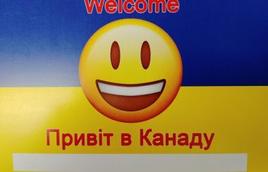 A picture of the welcome to Canada card. It has the yellow and blue colours of the Canadian Flag with a large smiley face. The card says welcome in both English and Ukrainian.