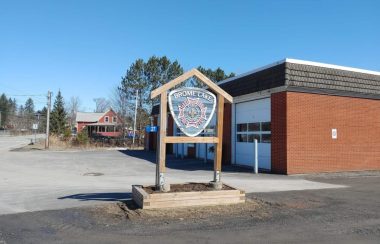 Picture is the front of the fire station in Brome Lake. It is a brick building with three large white garage doors with a sign that includes the fire department's emblem.