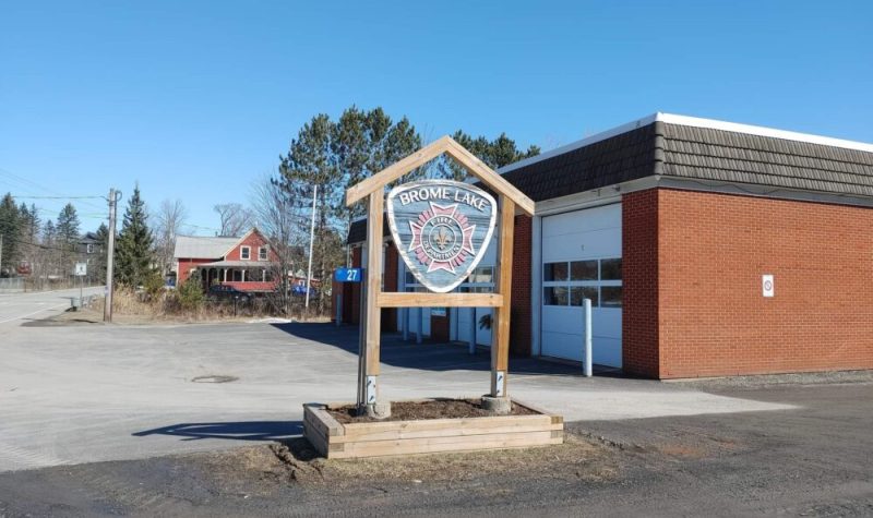 Picture is the front of the fire station in Brome Lake. It is a brick building with three large white garage doors with a sign that includes the fire department's emblem.