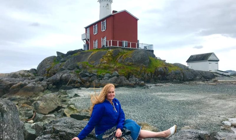 A woman smiles in front of a light house.
