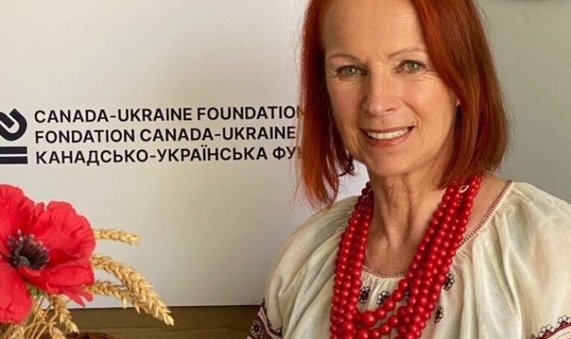 Pictured is Bohdana Zwonok with the Canada Ukraine Foundation logo behind her. She is sitting at a table with some of the meal items that will be available.