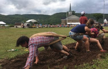 Une compétition de tir à la corde dans un champ avec une église au pieds des montagnes.