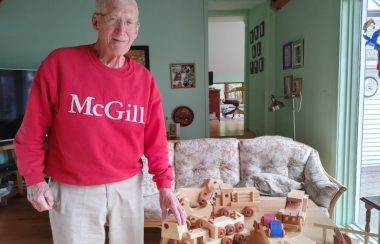 Pictured is Bob Pincott in his red McGill University sweater standing beside some of his wooden toys.