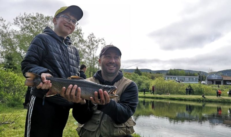 Un jeune garçon et son père tenant une truite à côté d'un lac.