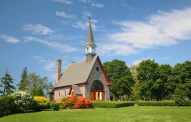 Une petite église en roches entourée d'arbres et de fleurs.