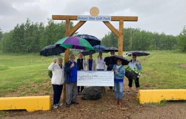 Une dizaine de personnes sont rassemblées derrière un chèque géant de 25 000 dollars à l'ordre du comté de Lac La Biche lors d'une journée pluvieuse.