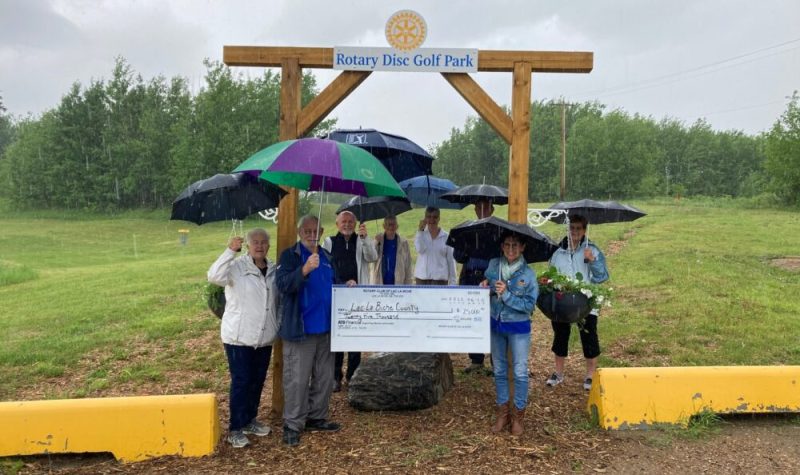Une dizaine de personnes sont rassemblées derrière un chèque géant de 25 000 dollars à l'ordre du comté de Lac La Biche lors d'une journée pluvieuse.