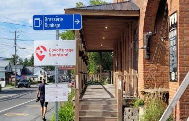 One of the Covoiturage Spontané ride-sharing stops in Dunham. It is a white sign with red writing and a hand with a thumbs up.