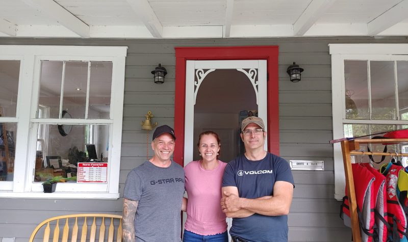 From left to right is Michel, Nancy, and Marc, standing in front of the check-in house at Les Minis. The building is grey with a red and white door.