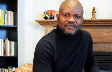 L'écrivain Blaise Ndala assis dans son salon entouré d'objets familiers