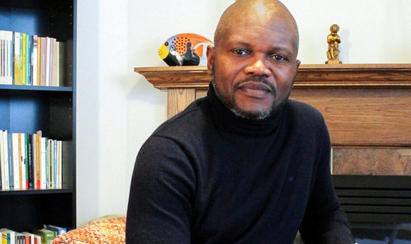 L'écrivain Blaise Ndala assis dans son salon entouré d'objets familiers