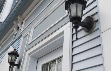 Two light fixtures on each side of a door frame outside of a blue building. The light bulbs are covered.