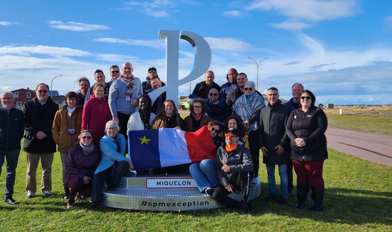 Une partie de la délégation accompagnant la SNA à Saint-Pierre et Miquelon. Une vingtaine de personne pose devant le logo de Saint-Pierre.