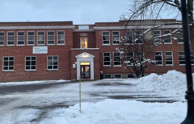 The front of a two story elementary school. It is a brick building with large windows that have white trim. There is snow in front of the school.