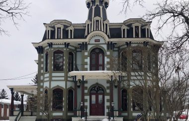 The building that houses Main dans la Main. It is an old Victorian style house. Its colours are white, beige, and maroon red and it has large windows.