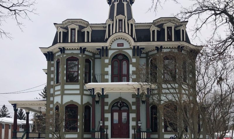 The building that houses Main dans la Main. It is an old Victorian style house. Its colours are white, beige, and maroon red and it has large windows.