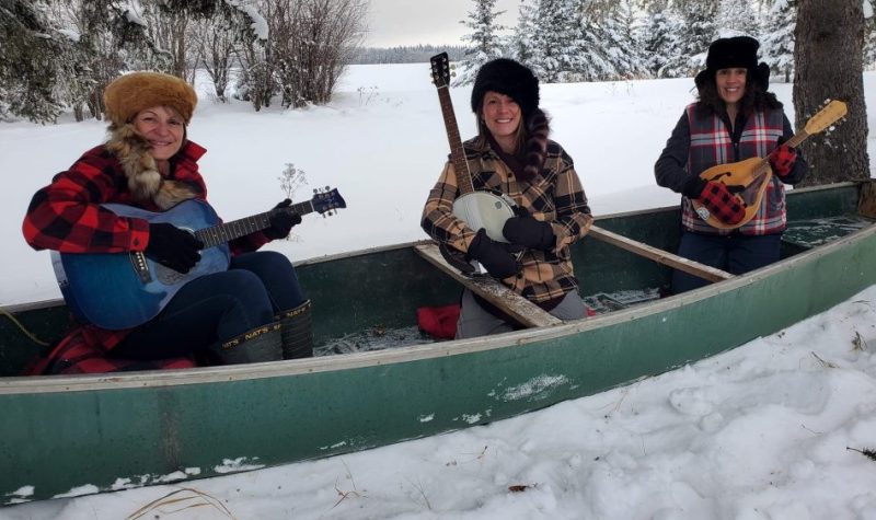 Trois femmes, guitares à la main, sont assises dans un canoë, un jour d'hiver.